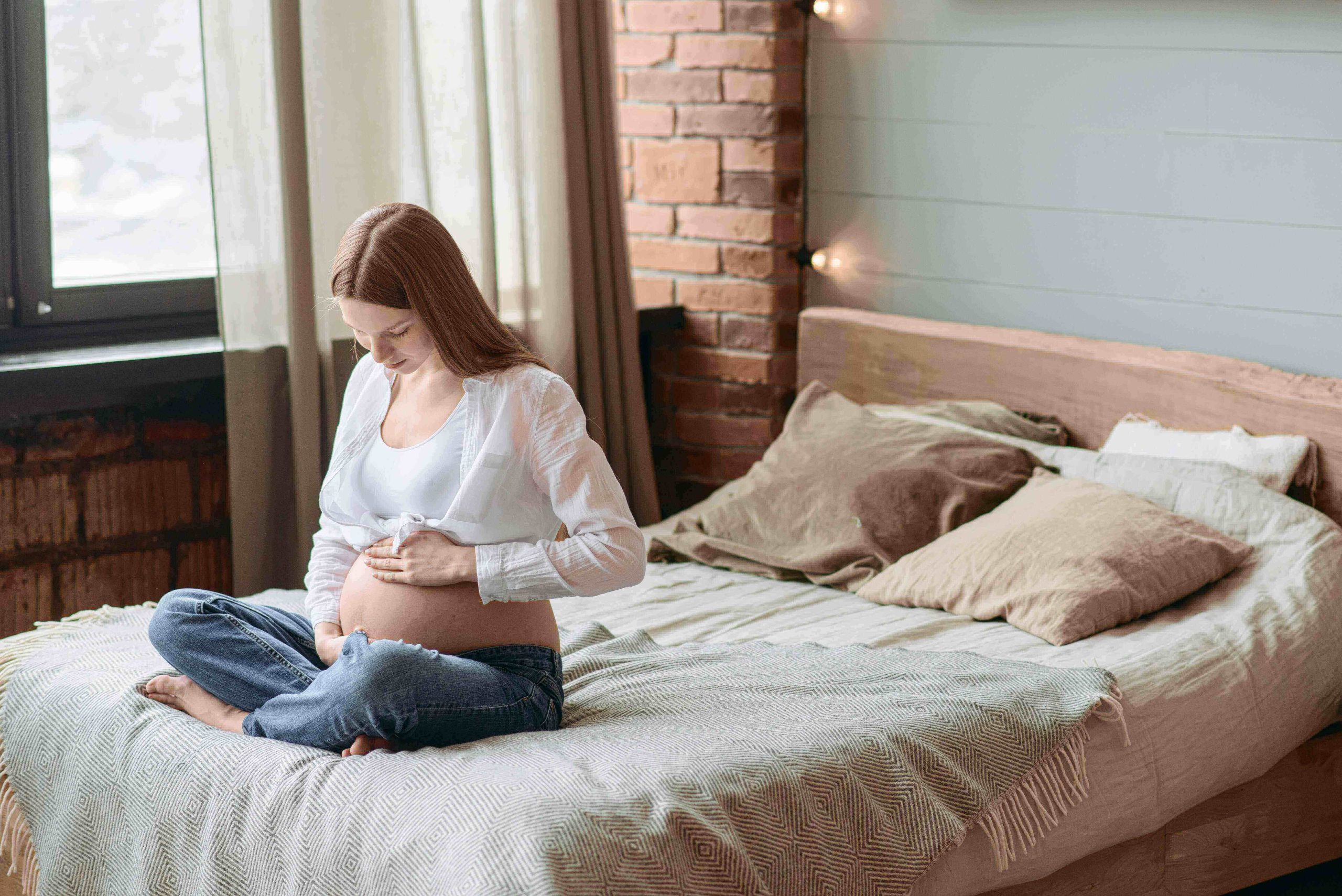 A pregnant woman is sitting on a comfortable mattress